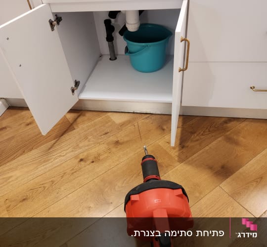כלי עבודה אדום על רצפה ליד ארון פתוח עם דלי
